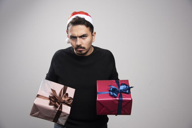 蝴蝶结一个戴着圣诞老人帽子的心烦意乱的男人手里拿着新年礼物包装男孩圣诞节