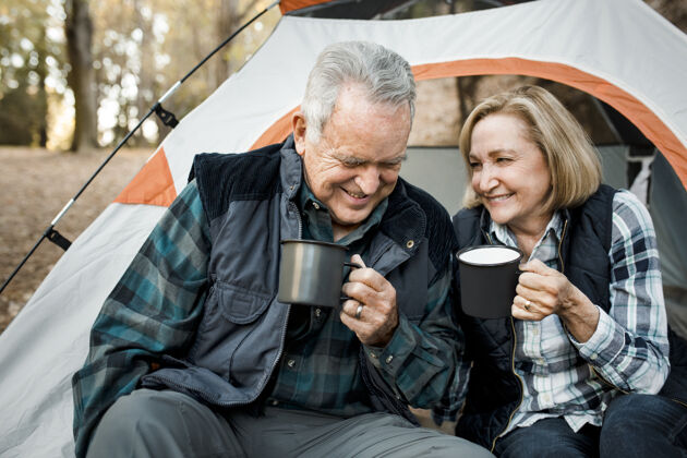 浪漫快乐的老夫妇在森林里的帐篷边喝咖啡冒险露营老年人