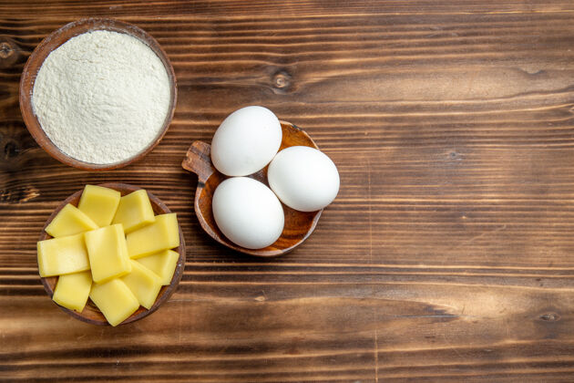 原料俯视整个生鸡蛋与面粉和奶酪在棕色桌上鸡蛋面团面粉粉尘产品灰尘视图面粉