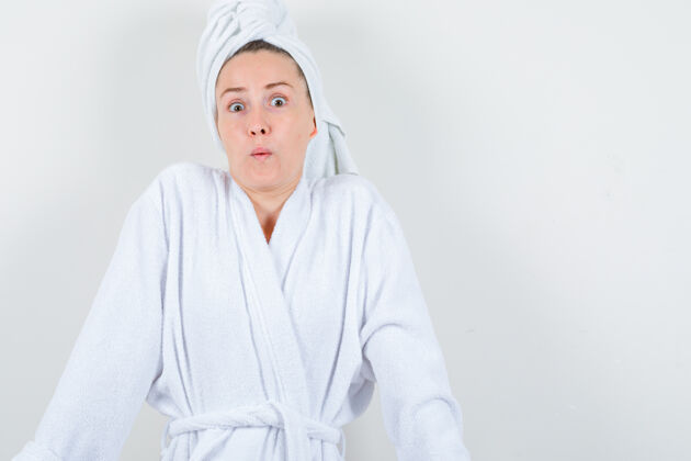 水疗穿着白色浴袍的年轻女士 毛巾显示出怀疑的姿态和困惑的神情 正面视图皮肤护理毛巾怀疑