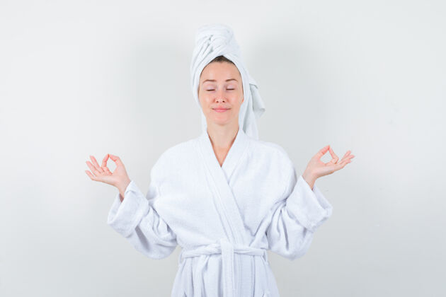 成人身穿白色浴袍的年轻女子 毛巾显示出冥想的姿势 看起来很放松 正面视图欢呼友谊室内