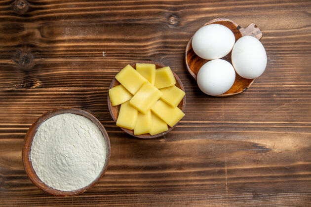 面粉俯视整个生鸡蛋与面粉和奶酪在棕色桌上鸡蛋面团面粉粉尘产品灰尘生的贝壳