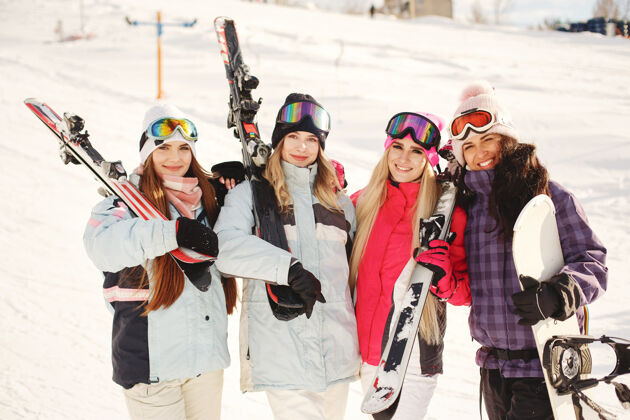 山腰女孩们手里拿着滑雪用具滑雪服上鲜艳的颜色女孩们在一起玩得很开心兴奋帽子站立