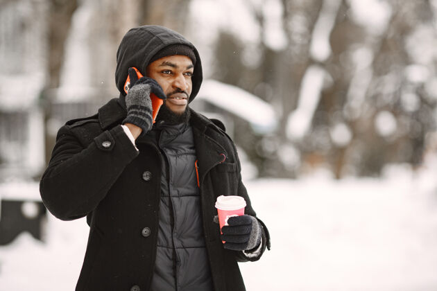 城市冬天小镇上的男人穿黑外套的男人拿着咖啡和电话的男人外套站外面
