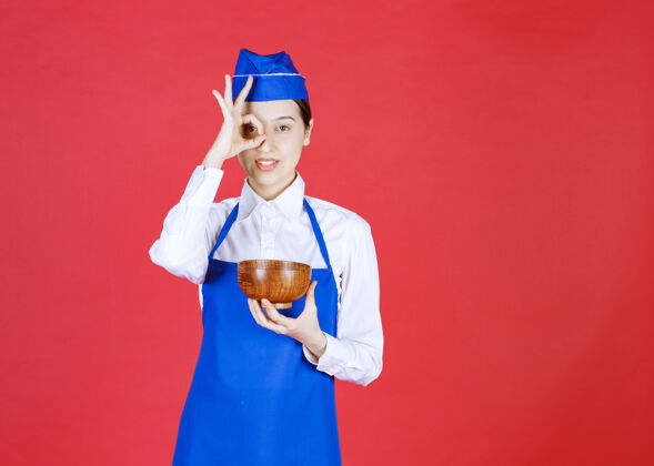 人类穿着蓝色围裙的亚洲厨师手拿一碗绿茶或面条 隔着手指看着女性日本人年轻人