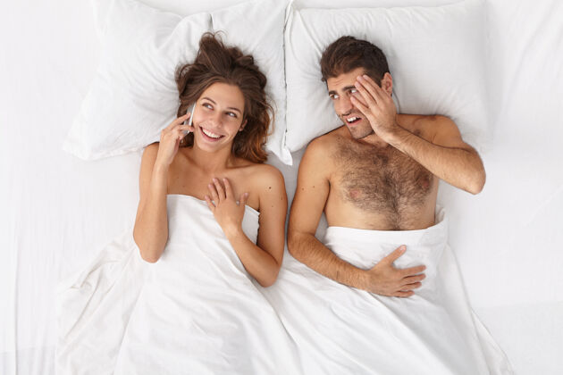 失望健谈的女人通过现代手机打电话 不理会躺在床上烦躁无聊的丈夫 需要沟通人 技术成瘾 关系观念醒来手机年轻