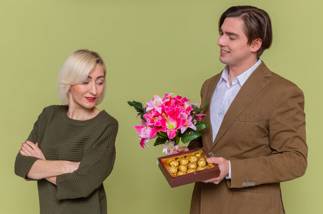 情侣年轻漂亮的夫妇幸福的男人送一盒巧克力糖果和一束鲜花巧克力花年轻人