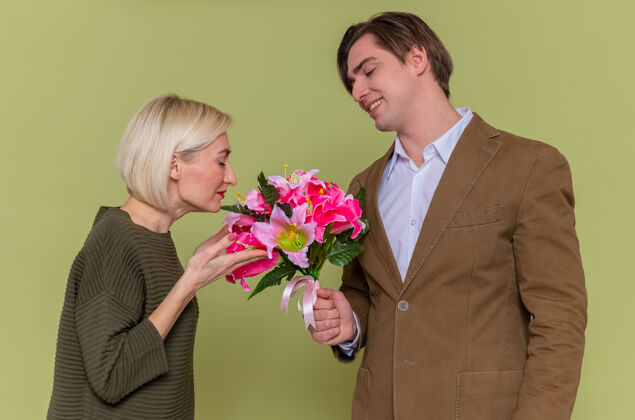 快乐年轻漂亮的情侣幸福的男人站在绿色的墙上给他可爱的女友送上一束鲜花庆祝国际妇女节立场国际美丽