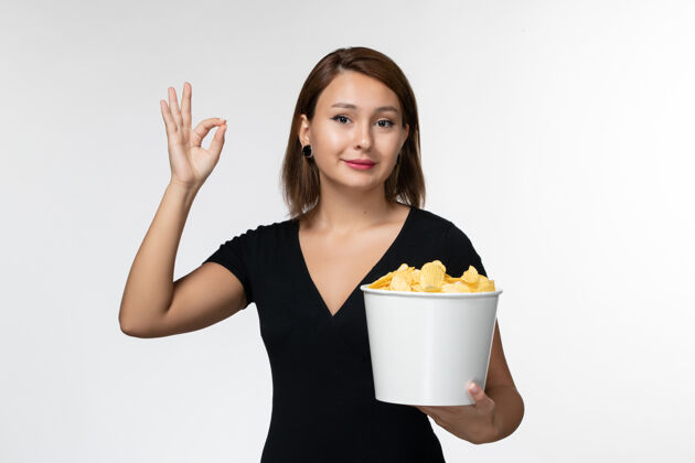 家庭主妇正面图身穿黑色衬衫的年轻女性手持薯片 在白色表面摆姿势衬衫漂亮前面