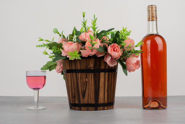 玫瑰美丽的花束和一瓶玫瑰红酒摆在灰色的桌子上花束叶子自然