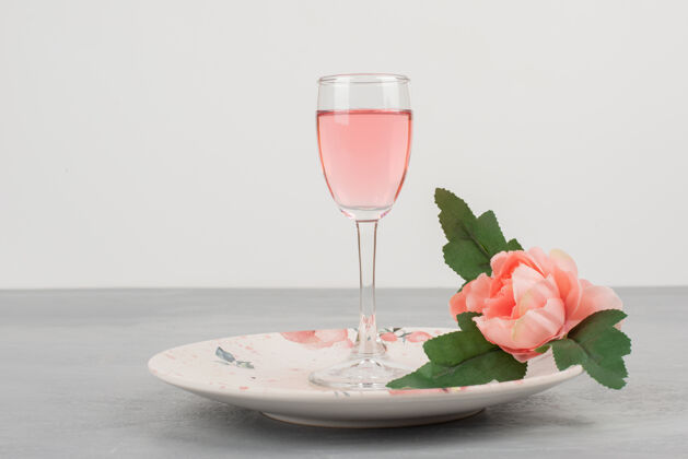盘子鲜花 盘子和一杯玫瑰红酒放在灰色的表面上花玫瑰酒
