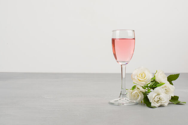 酒白玫瑰和一杯玫瑰酒摆在灰色的桌子上花婚礼花