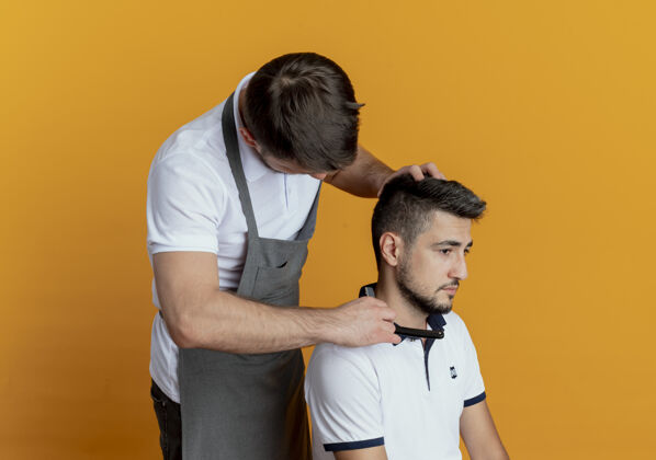剃刀穿着围裙的理发师用满意的顾客剃须刀在橘色墙上刮胡子顾客男人满意