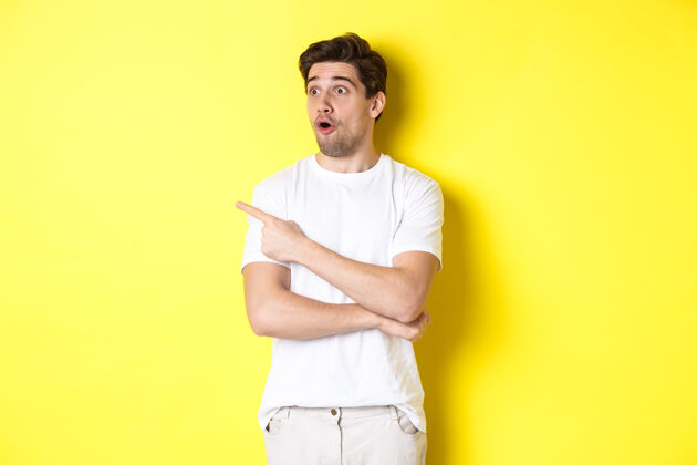 黄色一个穿着白色t恤的男人站在黄色的背景下 看着并用手指着宣传片 查看广告帅年轻自信