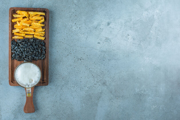 美味土豆条 葵花籽和一杯啤酒放在一块板上 蓝色背景种子薯条酒精