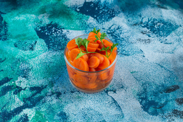美味把胡萝卜片放在杯子里 蓝色背景上玻璃胡萝卜蔬菜