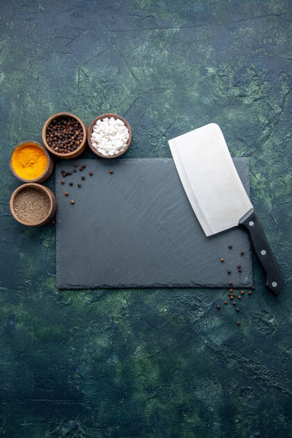盐顶视图不同调味品用大刀在深蓝色的食物表面撒上调味料盐胡椒的照片颜色香料利器板