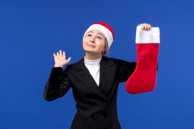 公司正面图：年轻女子手持红色圣诞袜在蓝色墙壁上过年人年轻女性圣诞节