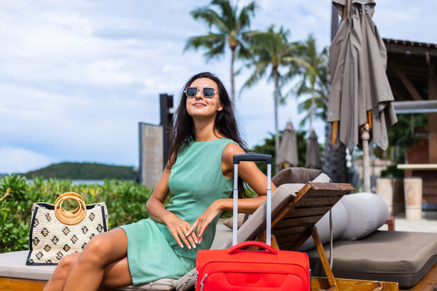 情感快乐的白种人漂亮的长发优雅的旅游女人在酒店外面穿着红色的手提箱夏天旅游度假