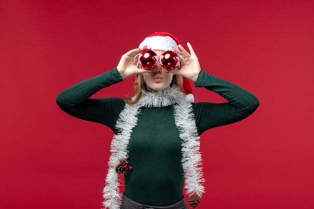 圣诞节正面图：年轻女性拿着圣诞树玩具站在红桌子上羽绒服装肖像