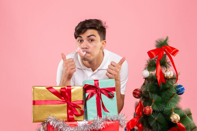 粉色前视图年轻人周围的圣诞礼物和节日树上的粉红色背景圣诞正面成人