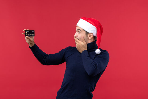 圣诞正面图年轻男子手持红色背景的黑色银行卡套装肖像红色