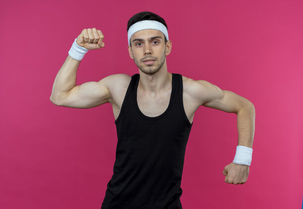头带戴着头巾的年轻运动型男子 摆出一副举起拳头的姿势 二头肌凌驾于粉色之上展示拳头粉红