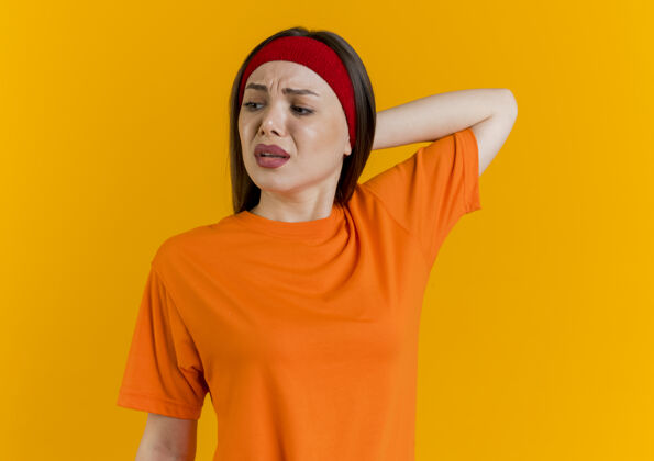运动戴着头带和腕带的未被释放的年轻运动女性看着侧面 手放在脑后壁板年轻橙色