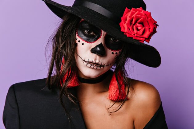 花墨西哥女士的特写肖像 她为“万死之日”化妆戴着红色配饰的女人在淡紫色的墙上摆姿势颜料女女巫
