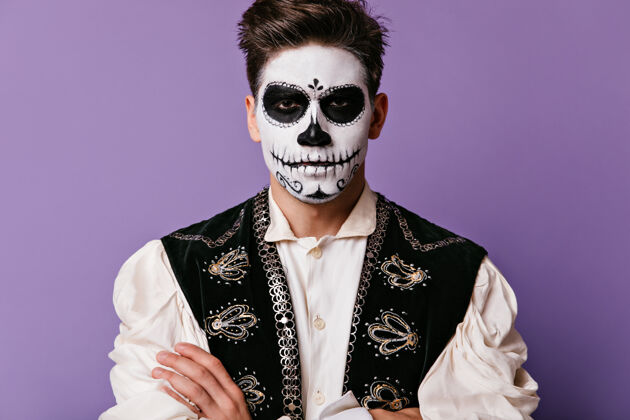 歌手一个戴着骷髅面具的严肃的男人在隔离墙上摆姿势一个穿着黑色背心 绣着刺绣的家伙五颜六色角色墨西哥