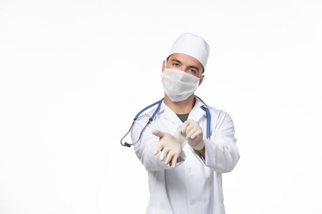 视图正面图：男医生穿着医疗服 戴着防毒面具 在淡白色的墙壁上传播病毒佩戴浅白色制服