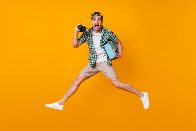 行李一个穿着夏季服装的有趣的游客 手里拿着复古相机和蓝色手提箱一个戴着潜水面具的人在橙色的空间里跳跃使机票休闲