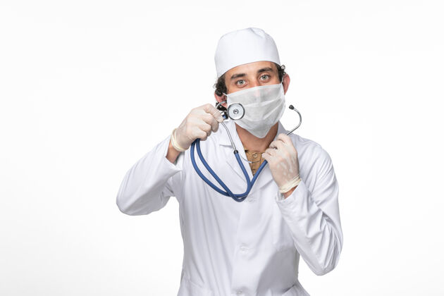 面罩前视图：男医生穿着医疗服 戴着口罩 防止白墙病毒冠状病毒大流行时戴着冠状病毒听诊器防护大流行持有