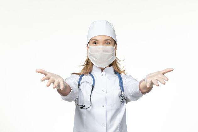 浅白色前视图：女医生穿着医疗服 戴着口罩和手套 因为冠状病毒正在欢迎轻型白墙病大流行的冠状病毒冠状病毒防护套装女性
