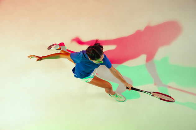 影子身穿蓝色球衣的年轻女子正在打网球她用球拍击球室内射门 光线混合年轻 灵活 力量和活力顶视图比赛健康运动员