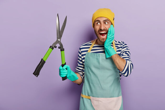 工具情绪维护工人拿着修剪剪 穿着工作服 剪树枝 隔离在紫色背景上大叫手套园艺