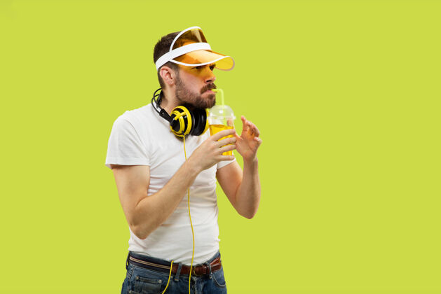 惊讶黄色空间中穿着衬衫的年轻人的半身特写肖像戴着耳机和饮料的男模喝酒迪斯科哇