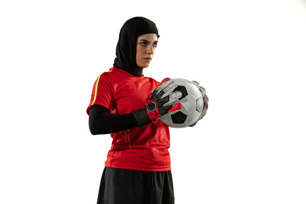 装备阿拉伯女足或足球运动员 守门员 背景为白色工作室年轻女子自信地摆出持球姿势 为球队进球保驾护航持球红色制服