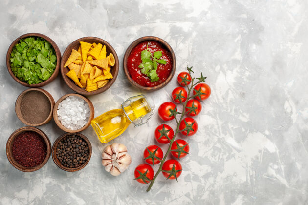 绿色俯瞰不同的调味品与绿色番茄和油在白色的桌子上番茄辣椒油