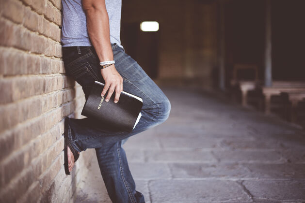 牛仔裤拿着圣经的人靠在砖墙上砖墙立场长凳