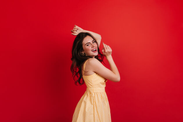肖像调皮的卷发女郎在红墙上跳舞身着黄色连衣裙的黑发女郎真诚地微笑着 喜欢拍照发型休闲可爱