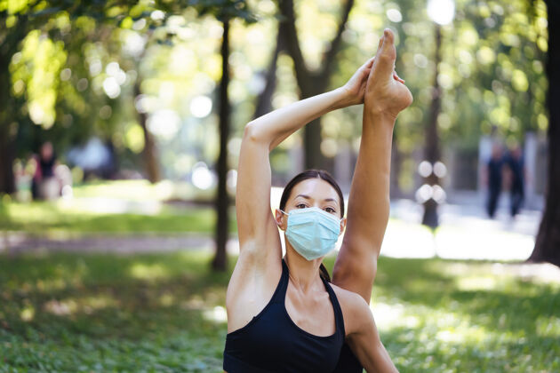 训练戴着医用防护面具的运动型年轻女子 早上在公园里做瑜伽 在瑜伽垫上进行女子训练面膜锻炼健康