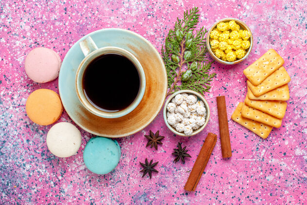 生的顶视图五颜六色的法国马卡龙肉桂饼干和一杯茶在粉红色的桌子上烤蛋糕甜甜的糖馅饼的颜色饮料茶派