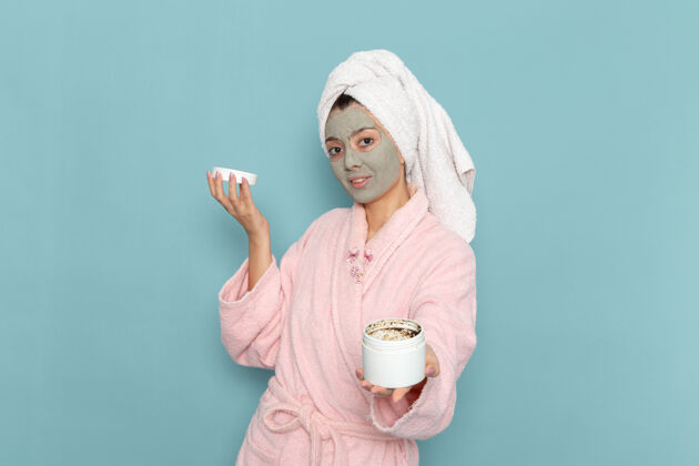 正面正面图穿着粉色浴袍的年轻女性 脸上戴着面罩 浅蓝色墙壁上有淋浴清洁美容自护霜人浴袍年轻人