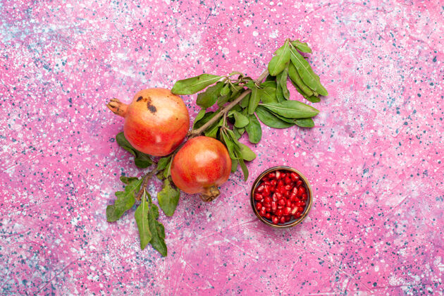 顶部顶视图新鲜石榴与绿色的叶子在粉红色的表面水果健康可食用的水果