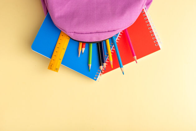 购物顶视图彩色铅笔与抄写本和紫色书包上的淡黄色书桌学校感觉笔铅笔本记事本毛毡视图钢笔