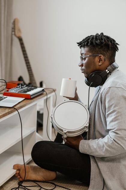 男侧视图男音乐家在家里打鼓和混合与笔记本电脑创造者耳机音乐家