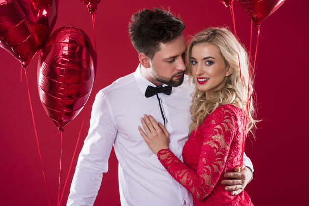 情人节一对迷人的夫妇手里拿着两串闪闪发光的红色气球气球面对面女性化