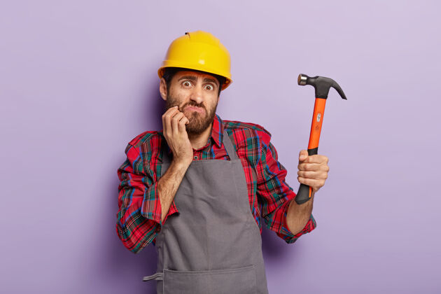 建筑工人家居装修概念愤愤不平的建设者手握铁锤 做装修头盔工人锤子