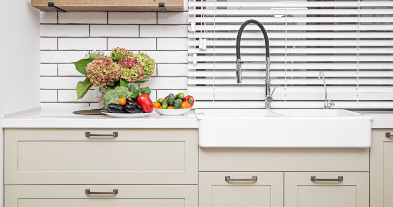 现代白色的厨柜 门上有金属把手 靠近洗脸盆 有一束鲜花和一盘蔬菜蔬菜室内新鲜